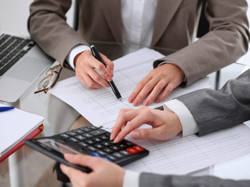Two female accountants counting on calculator income for tax form completion