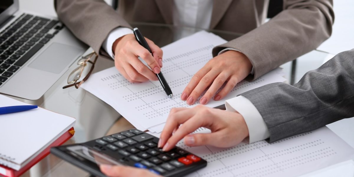 Two female accountants counting on calculator income for tax form completion