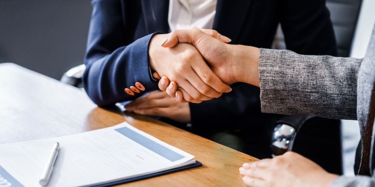 Two female lawyers in business suits shake hands at wooden desk, finalizing legal agreement. wooden gavel and scales represent justice as they discuss corporate law, compliance, dispute resolution.